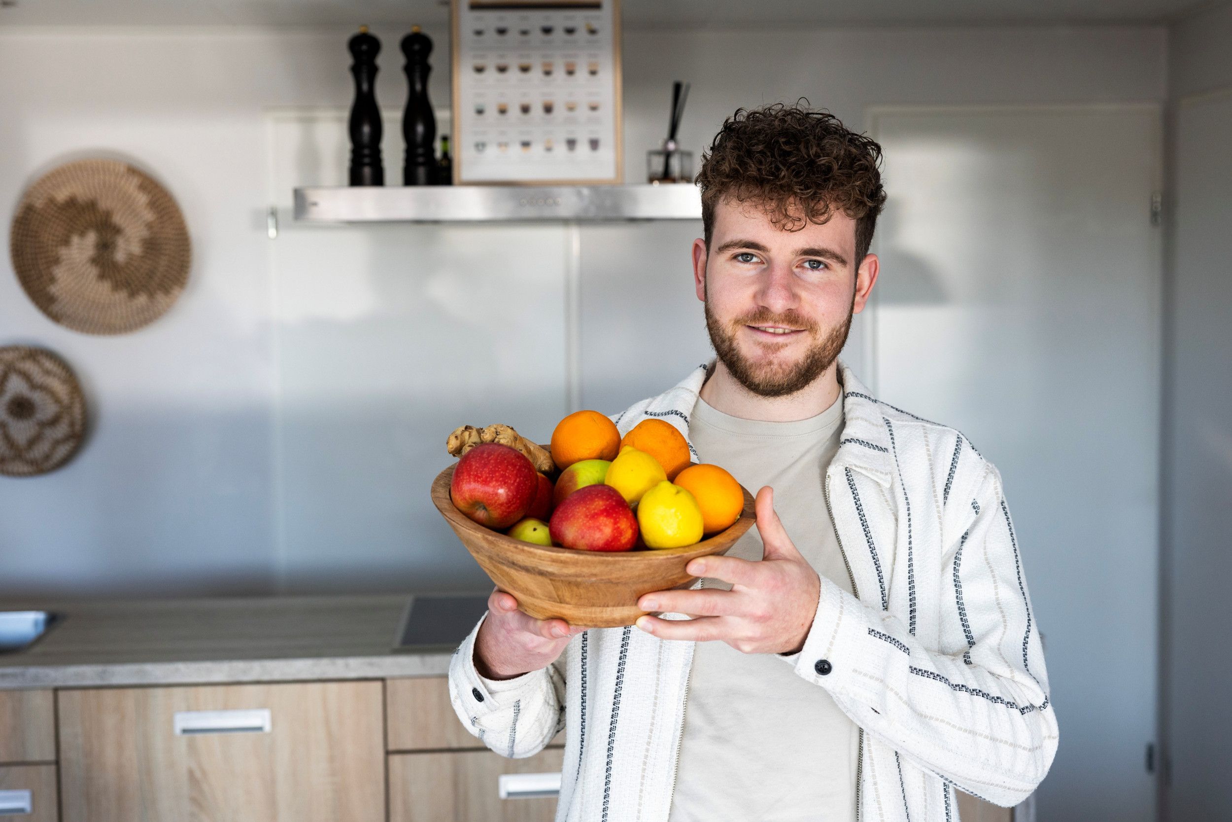 Een jonge man staat voor een aanrecht. In zijn handen houdt hij een schaal met fruit. Appels, sinaasappels en citroenen.
