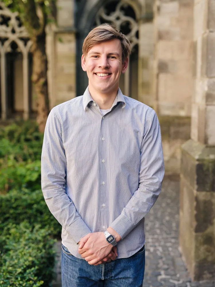 Een jongeman staat met zijn handen over elkaar en kijkt lachend in de camera.