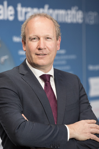 Een man in kostuum en stropdas kijkt met de armen over elkaar in de camera voor een portretfoto.