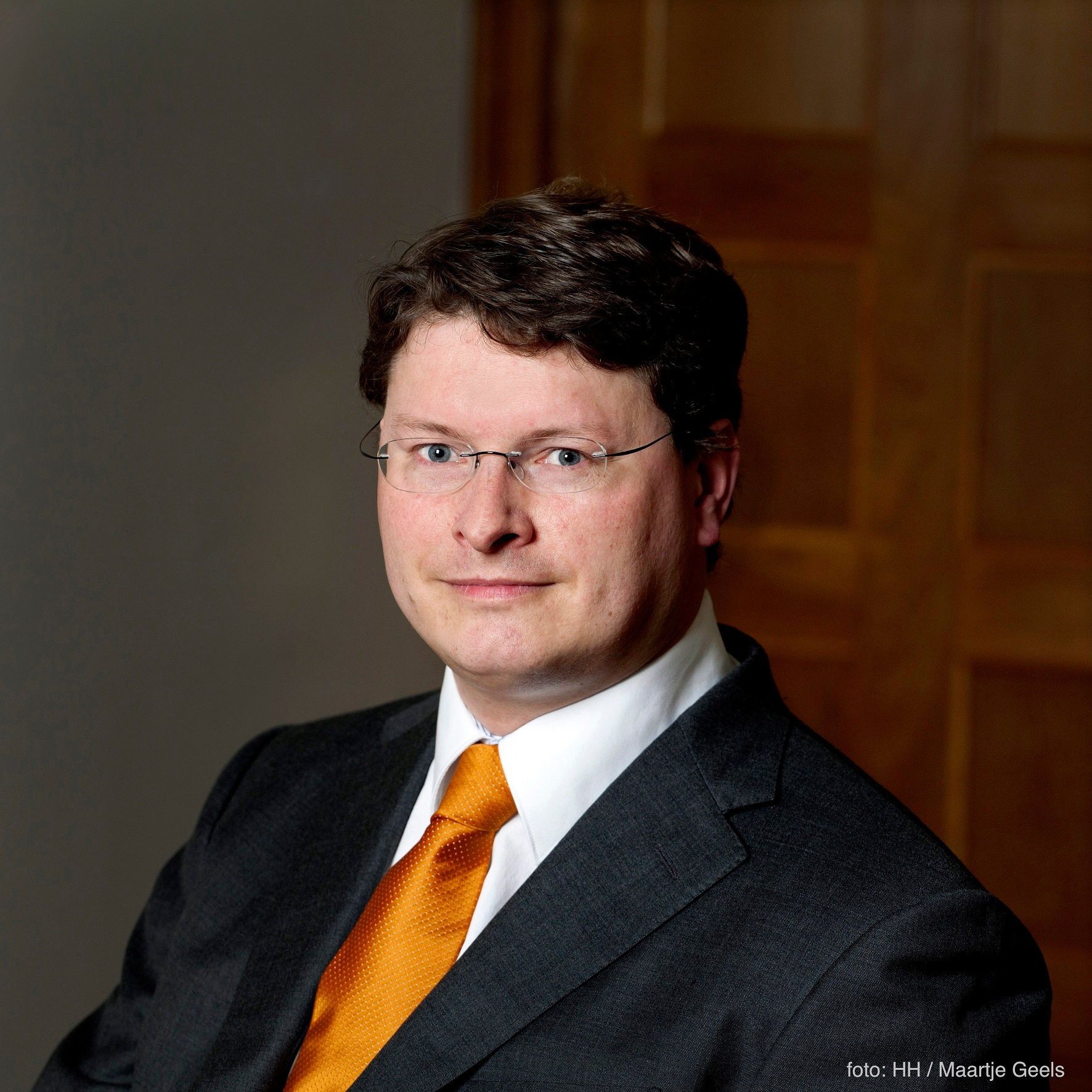 Man in pak met oranje das en bril.