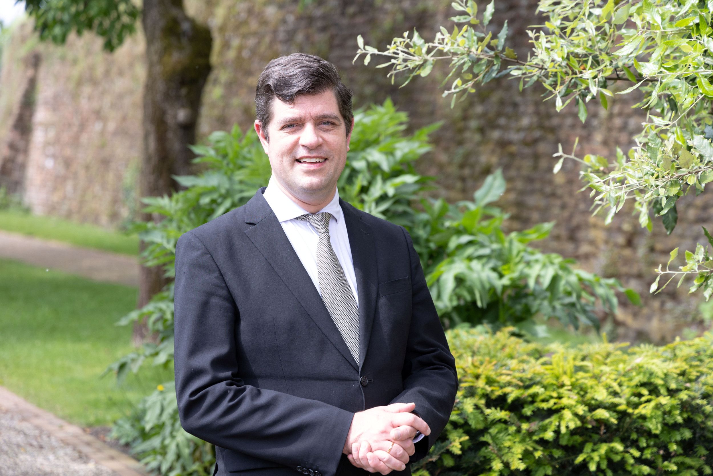 Predikant in zwart pak met stropdas staat in tuin.