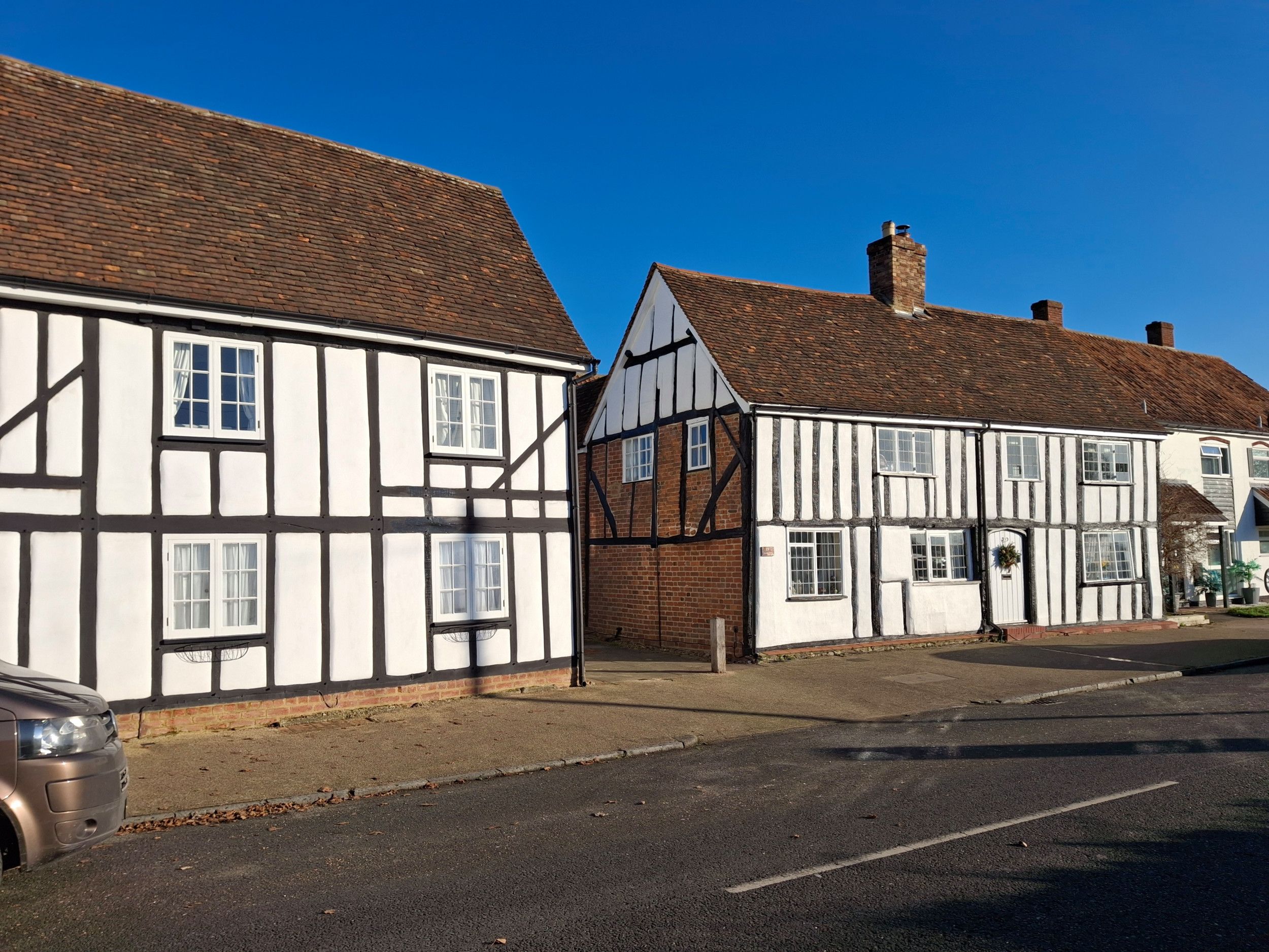 Een soort witte vakwerkhuizen aan een straat. Links nadert een auto.