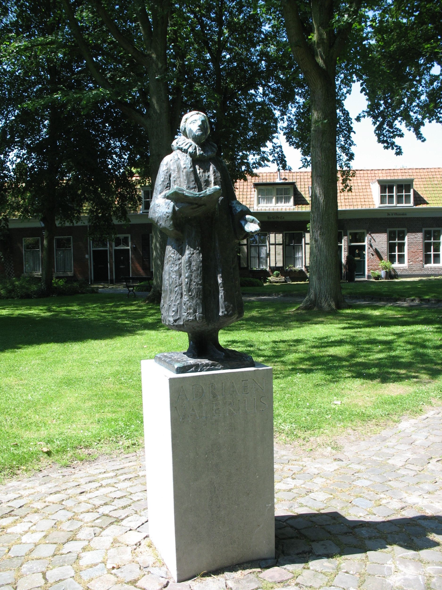 Bronzen standbeeld van Valerius, met een open boek in zijn hand, op een grijze sokkel.