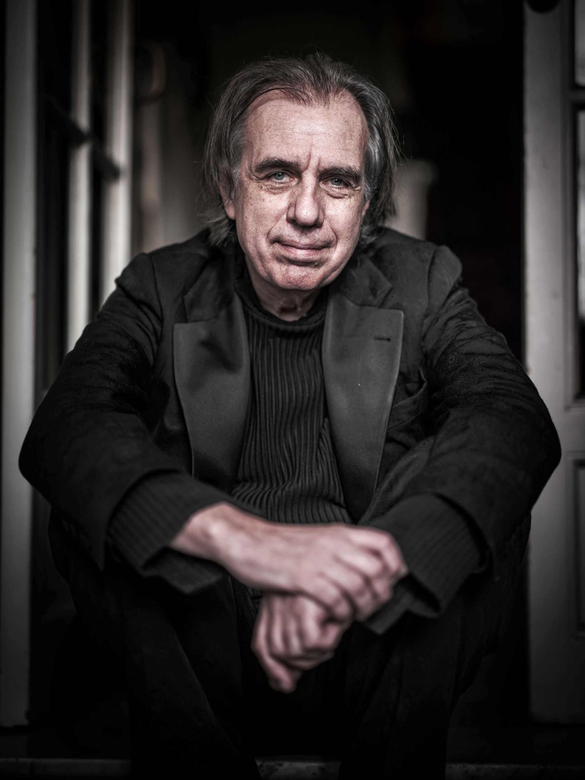 Close-up van man in het zwart die op een lage richel zit terwijl zijn armen op zijn knieën rusten.