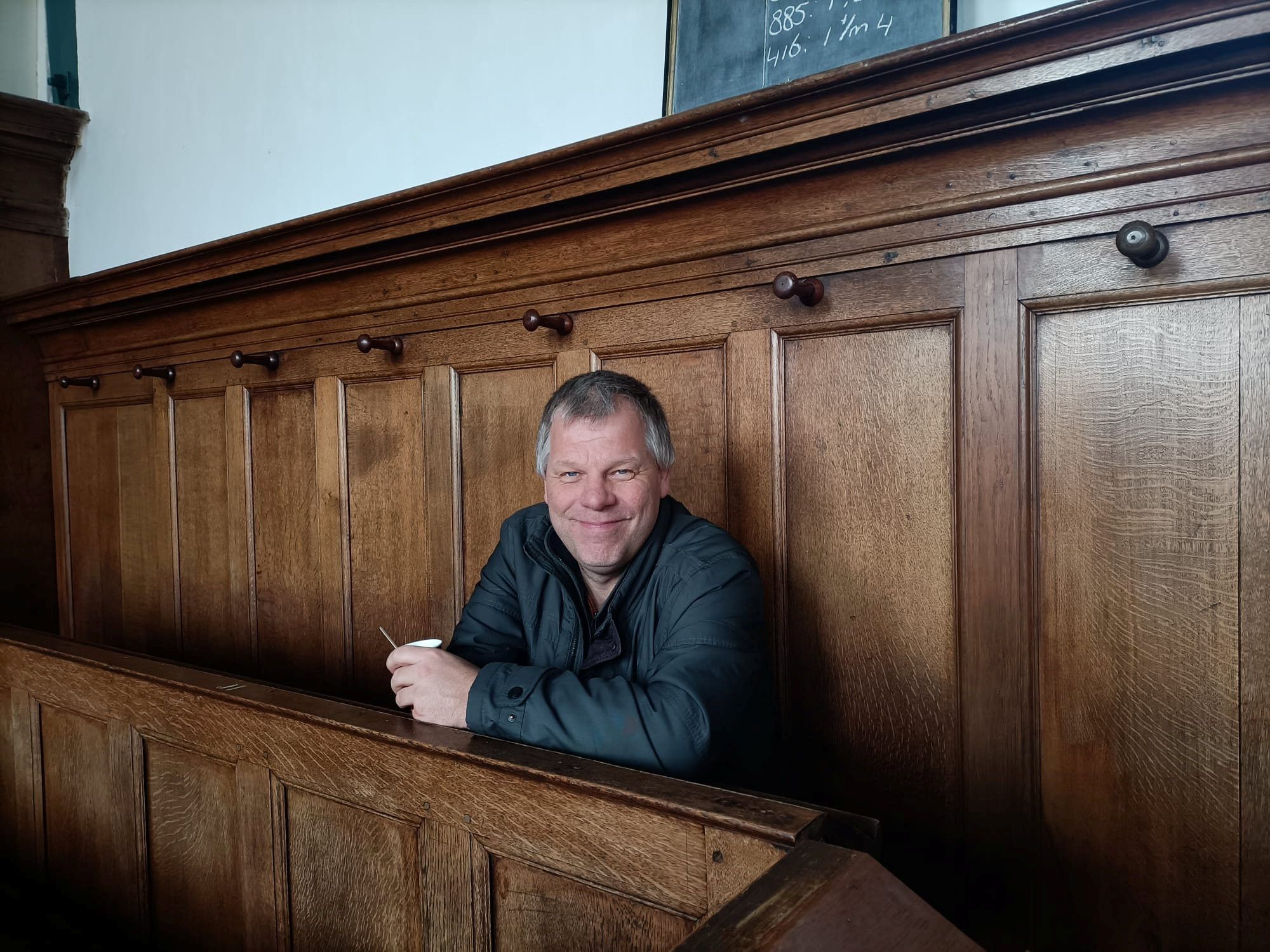 Een glimlachende man met grijzend haar in een oude kerkbank.