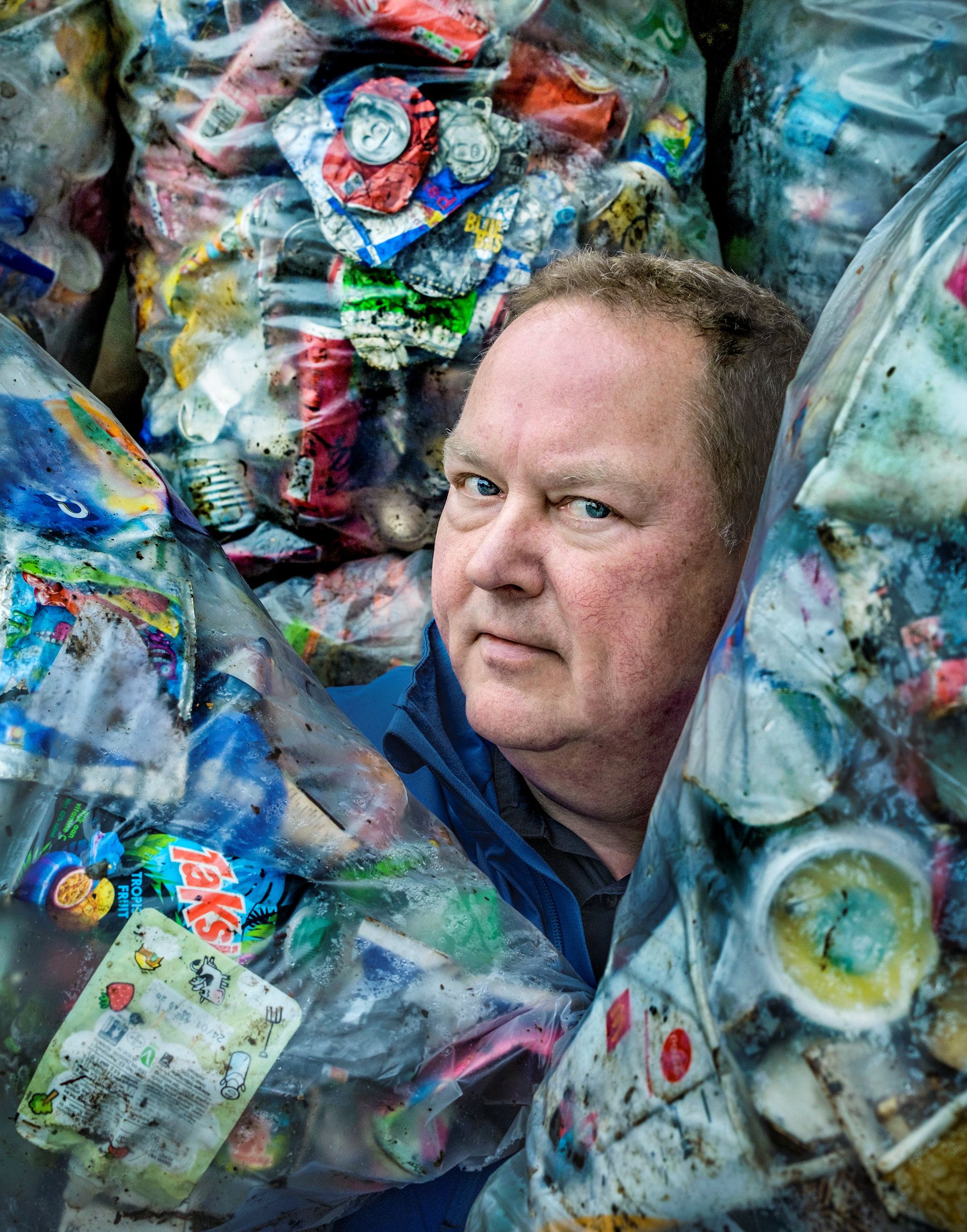 Een man steekt met zijn hoofd tussen allerlei zakken met zwerfafval uit. 