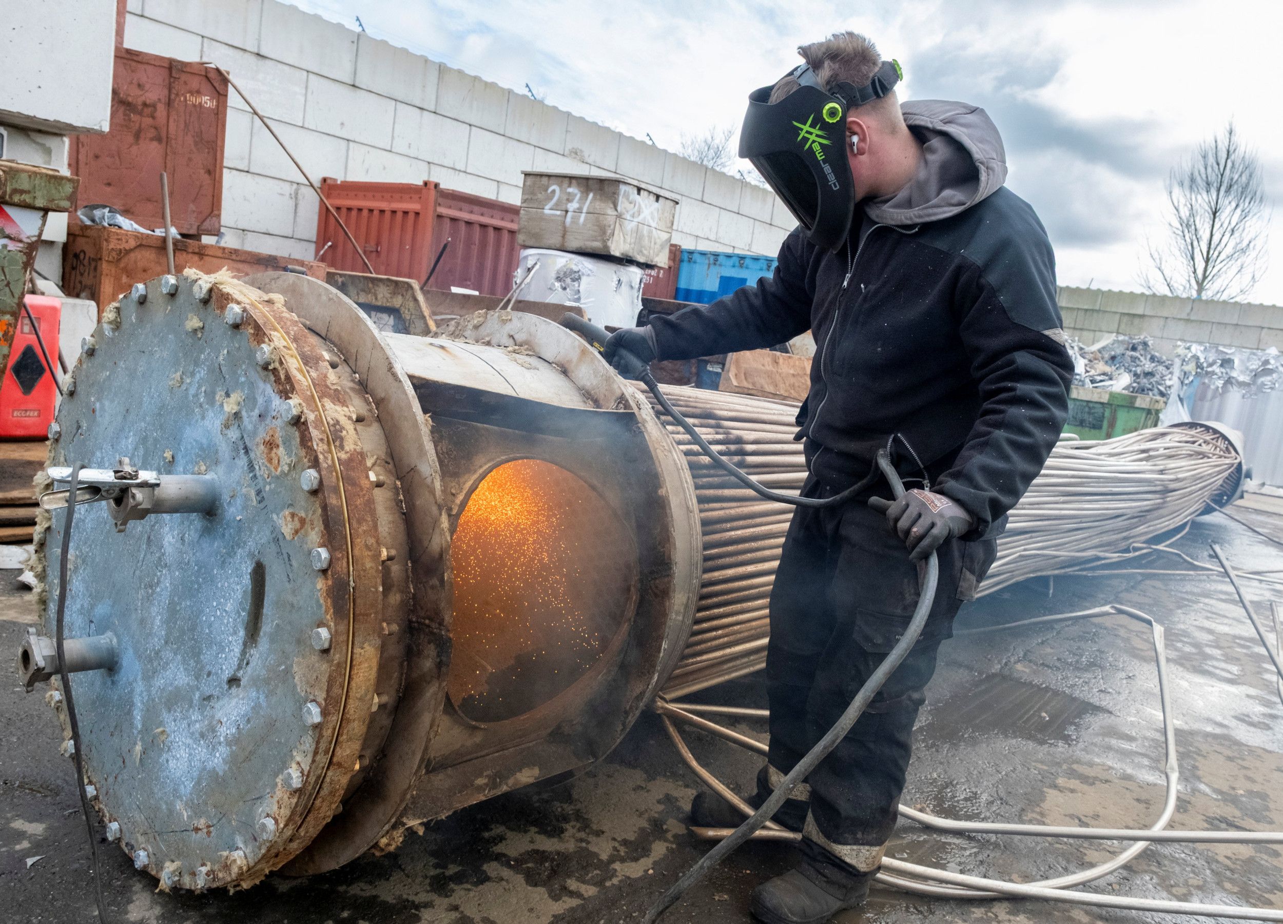 Man met laskap op zijn hoofd slijpt metaal weg bij een groot voorwerp met bundel dikke draden. 