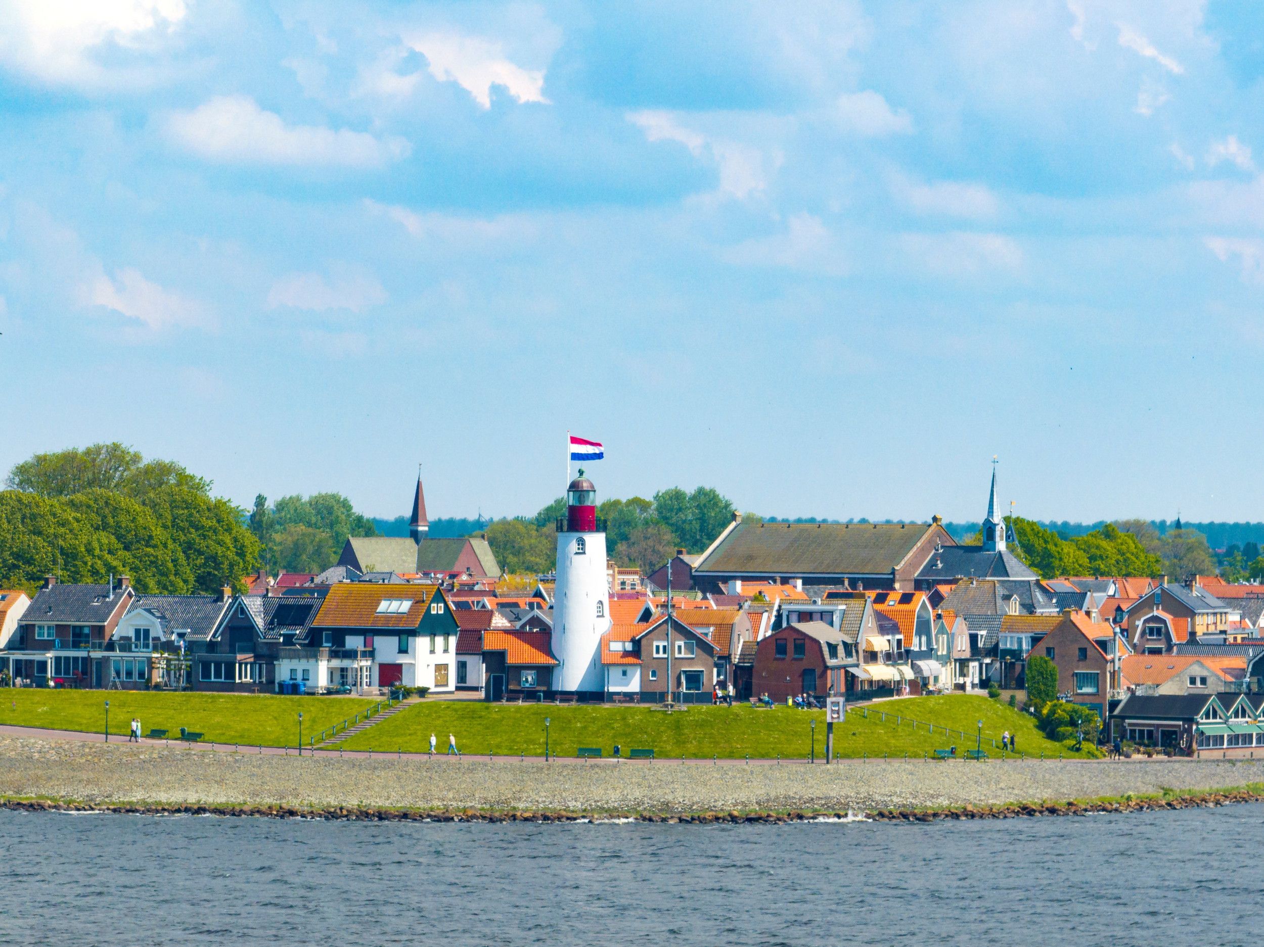 De witte vuurtoren van Urk met op de achtergrond woonhuizen en diverse kerkgebouwen tegen een blauwe lucht.