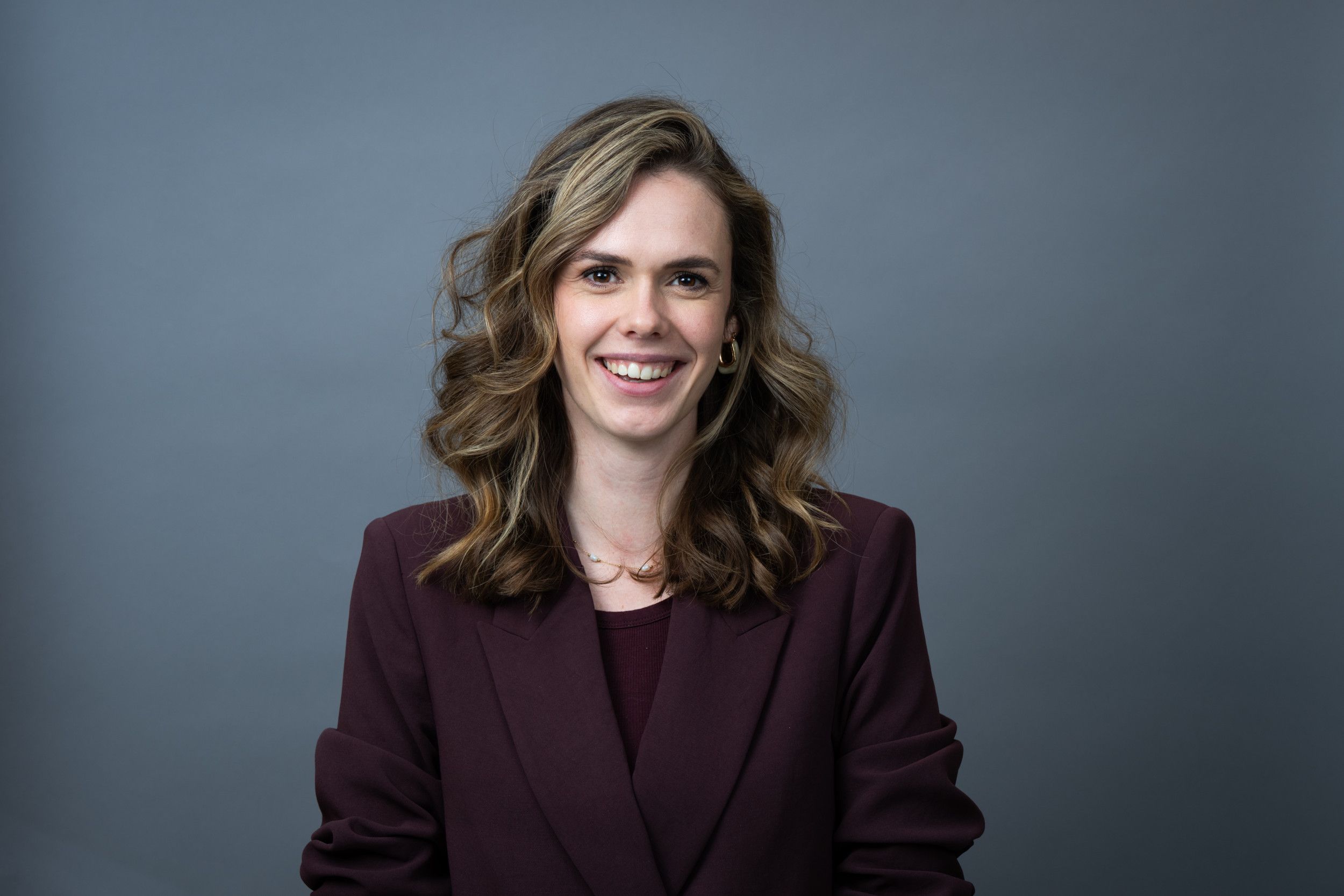 Vrouw met bruinblond krullend haar en donkerpaarse blazer. 