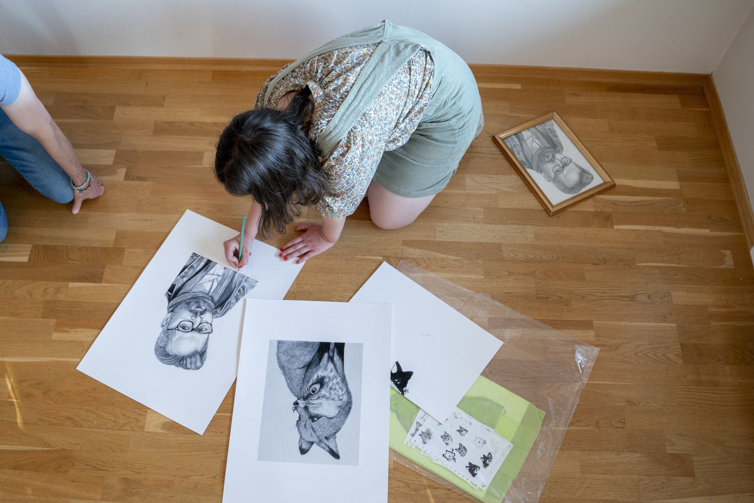 Een meisje met donker haar zet een handtekening onder een pentekening van een man met een baard.