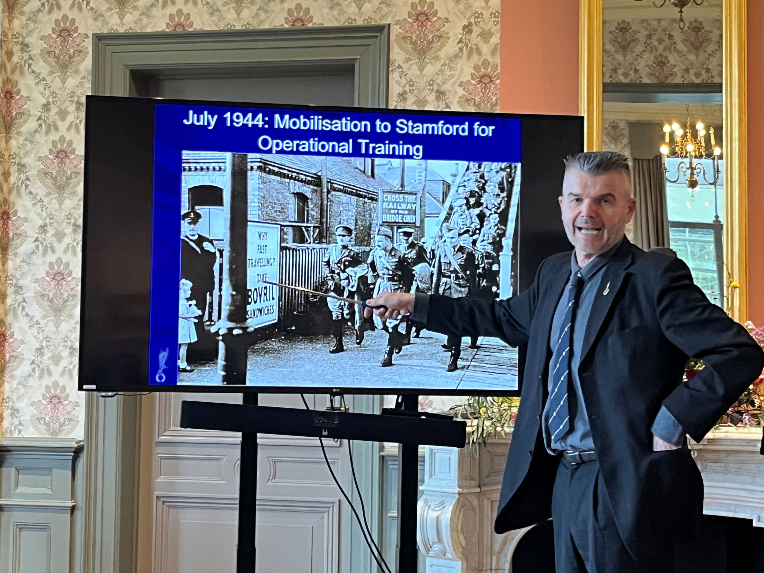 Een man wijst met een stok naar een foto.