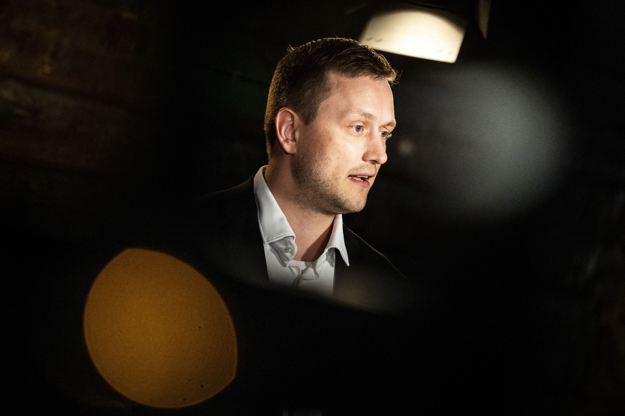 Blonde man in wit overhemd met donker colbert voor Groenlandse vlag.