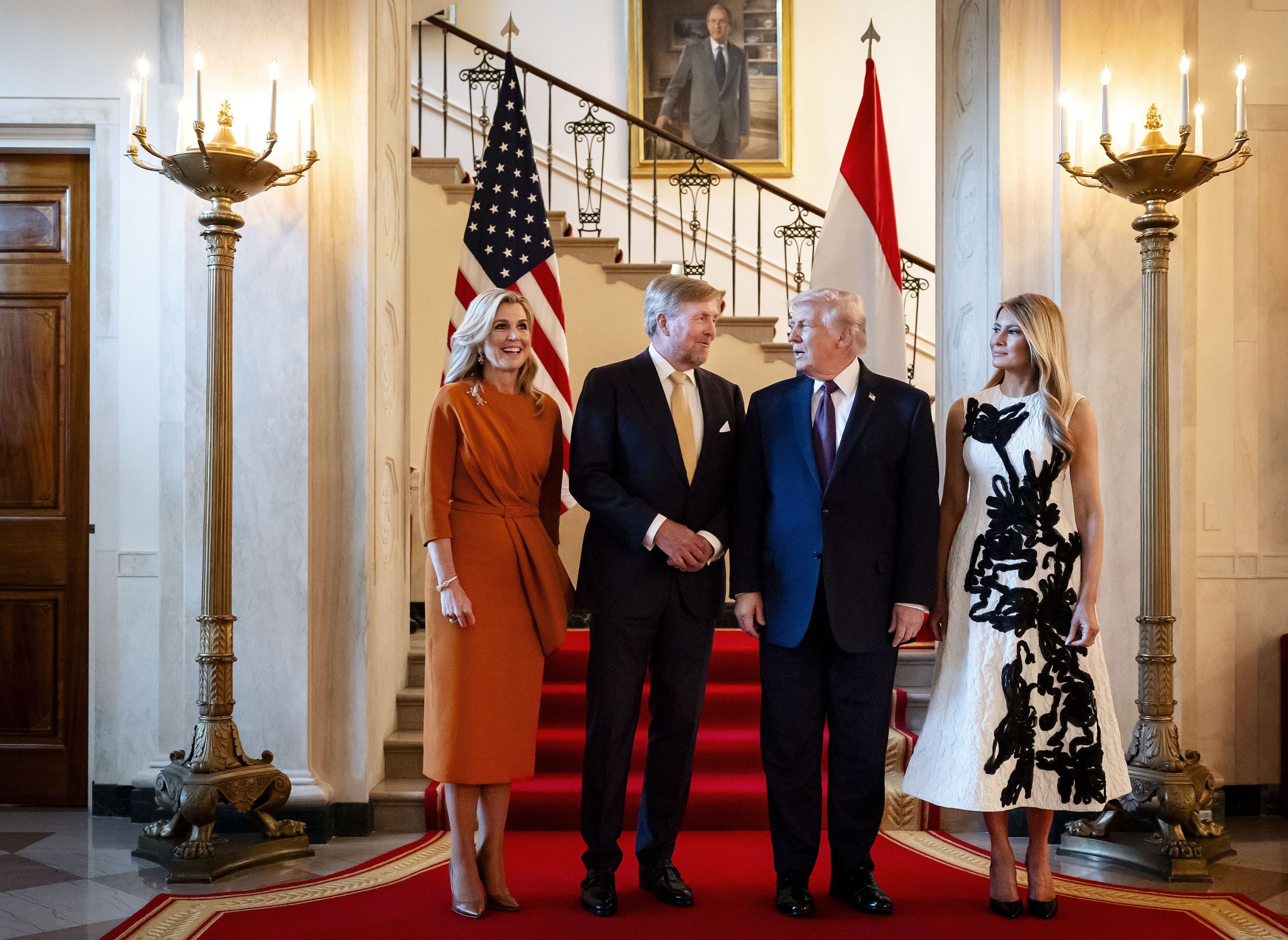 Mannen in een blauw pak praten met elkaar, twee vrouwen kijken glimlachend toe.