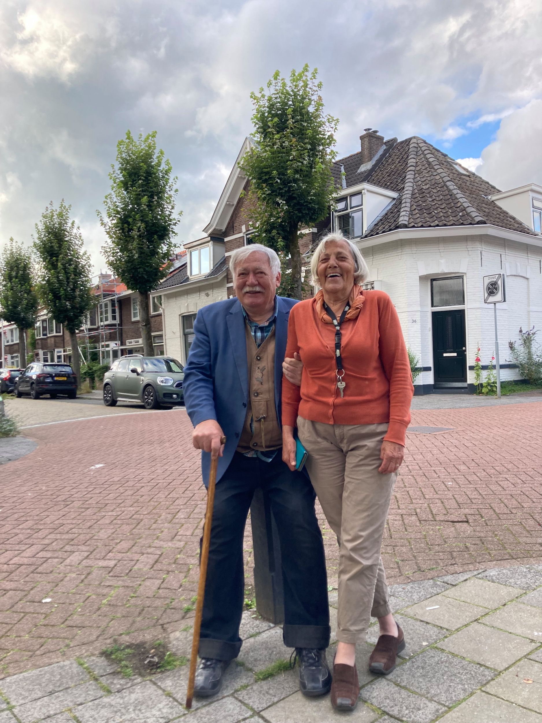 Een man met een stok zit op een paaltje en houdt zijn hand om de arm van zijn lachende vrouw.