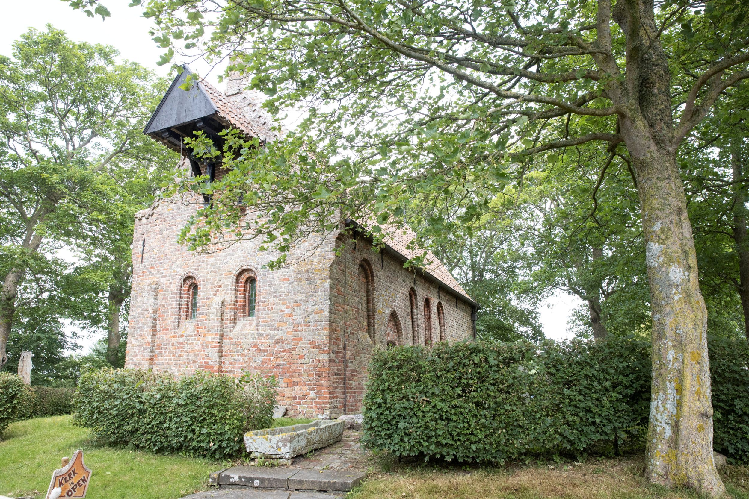 Een oud kerkje, omgeven door geboomte.