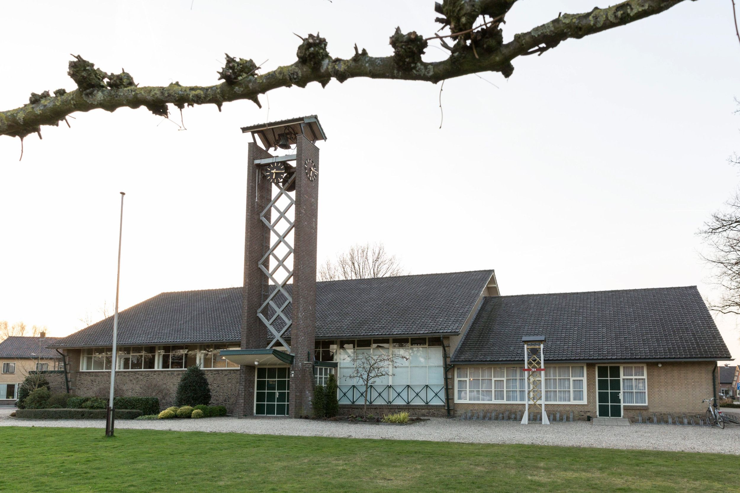 Een sober kerkgebouw, type lange schuur, met een hoge toren.
