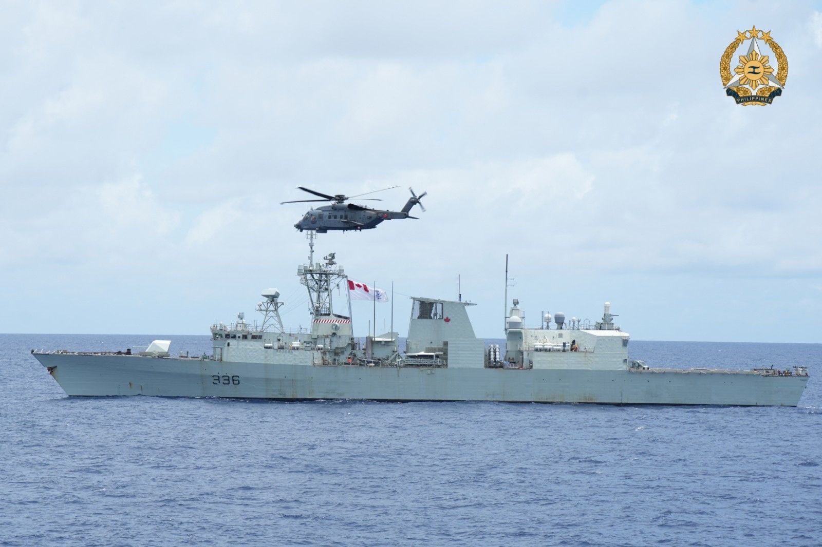 Militair vaartuig in oceaan, helikopter vliegt ervoor.